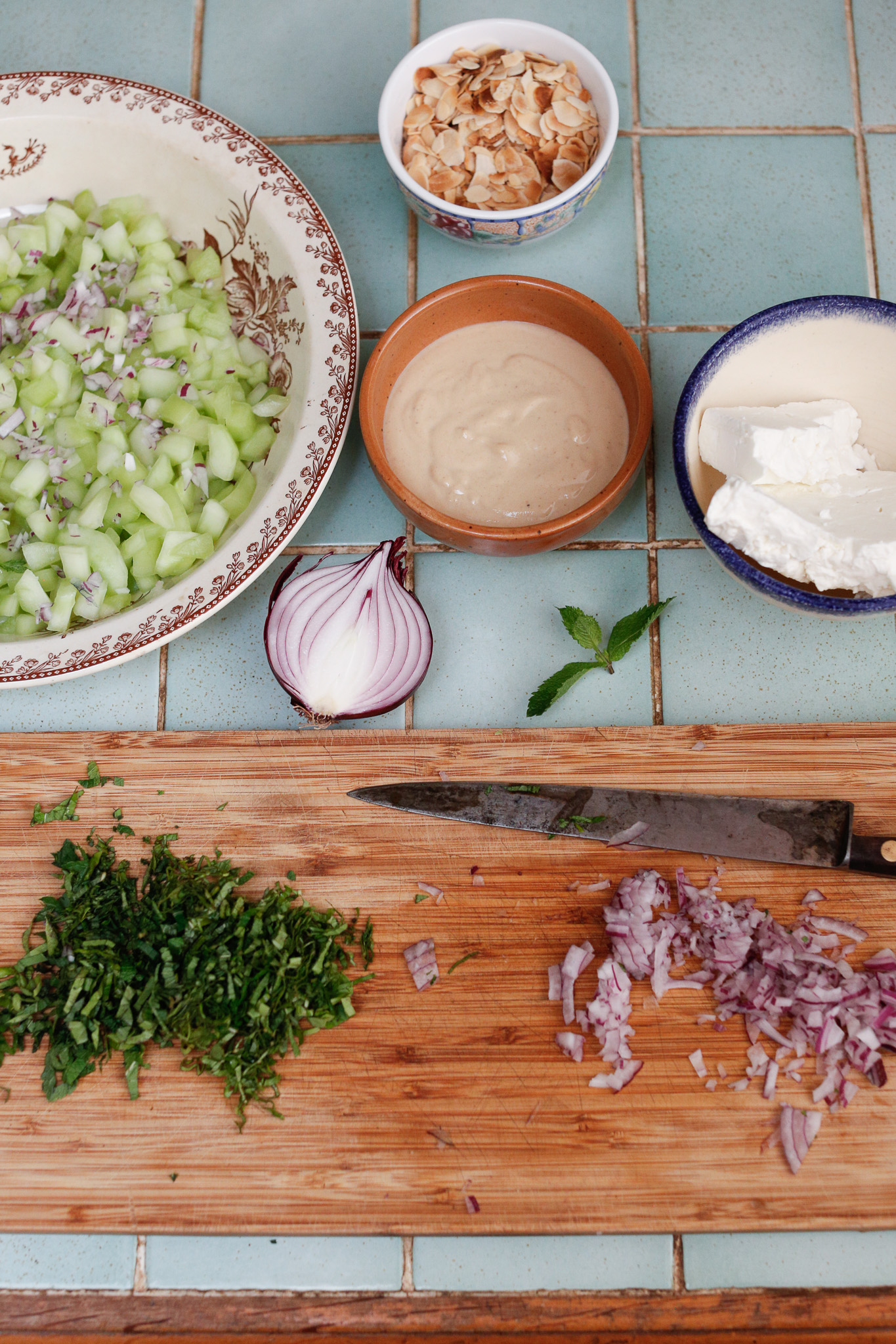 You have all your ingredients ready to layer now. Start with some cucumber, red onion, grapes, almonds, herbs and feta.