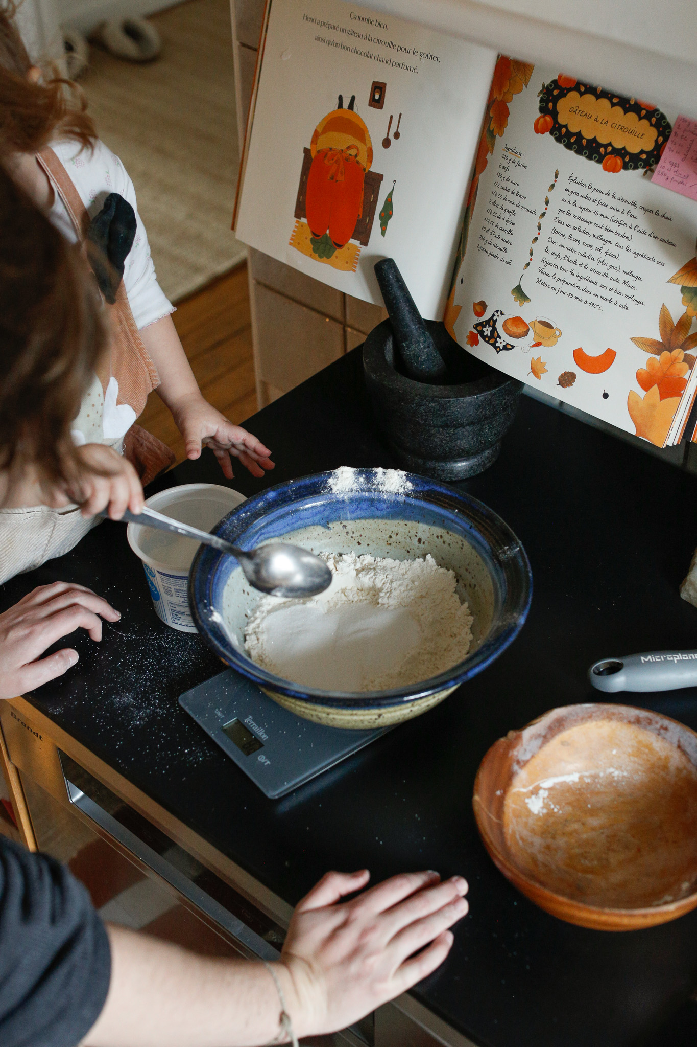 Uncle Alex monitoring the scale as Indhia adds flour spoonful by spoonful.