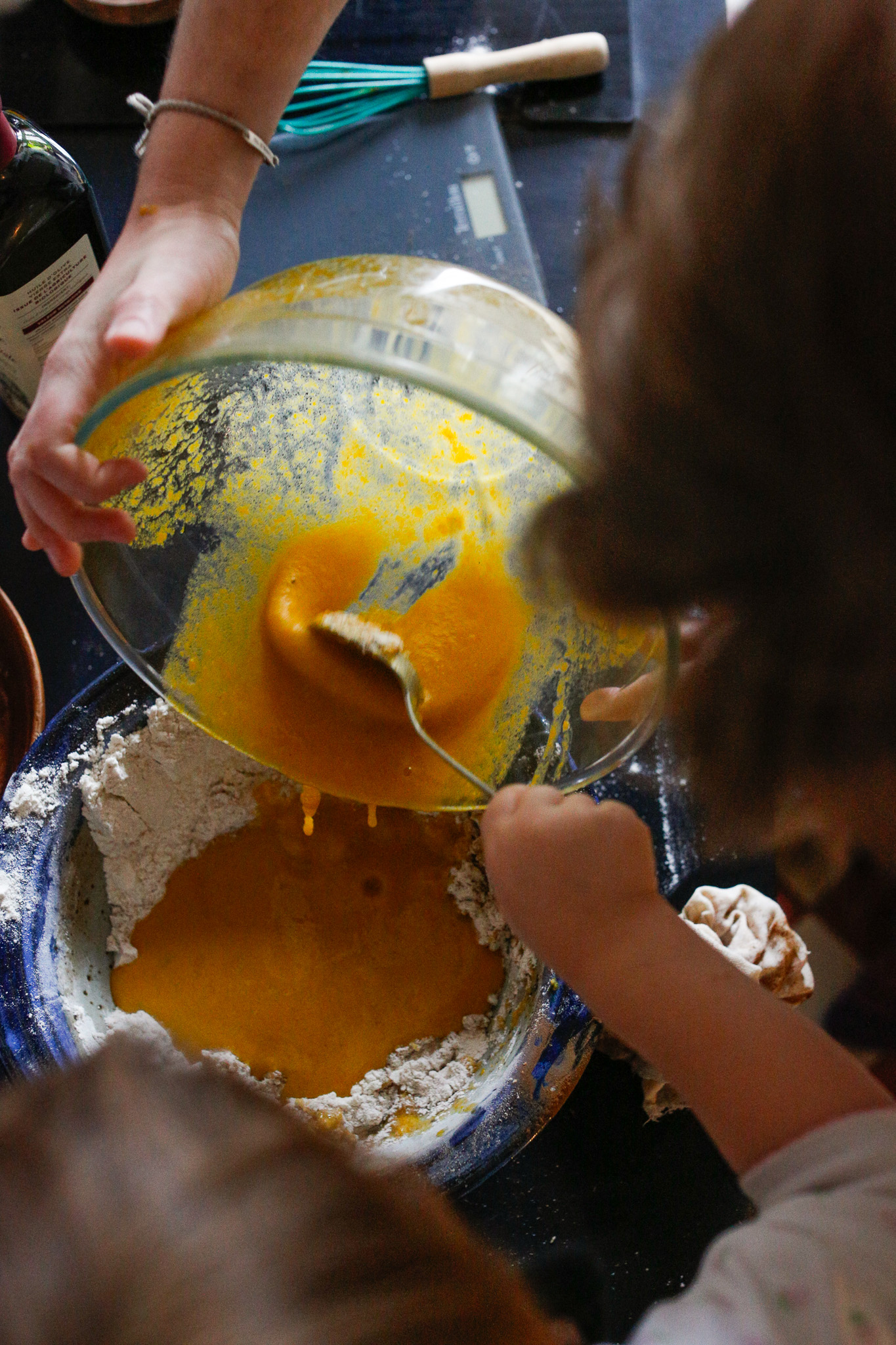 Uncle Alex holding the bowl and Indhia using a spoon to scoop it through. Use a rubber spatula to scoop the remainder of the batter into the pan.